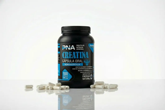 Cápsulas brancas de Creatina Monohidratada PNA espalhadas junto ao pote, suplemento prático para recuperação muscular.