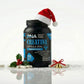 Frasco de PNA Creatina Monohidratada em cápsulas com um gorro de Pai Natal no topo, rodeado por cápsulas brancas espalhadas, azevinho e um sino dourado com laço vermelho sobre neve artificial.